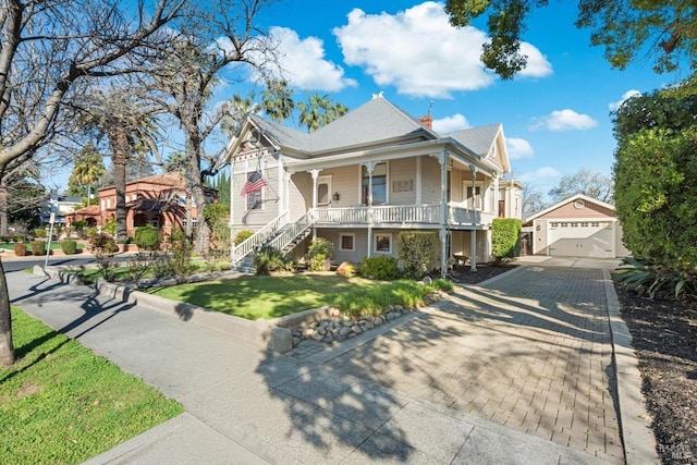 victorian home with a front yard, covered porch, a chimney, a garage, and an outbuilding