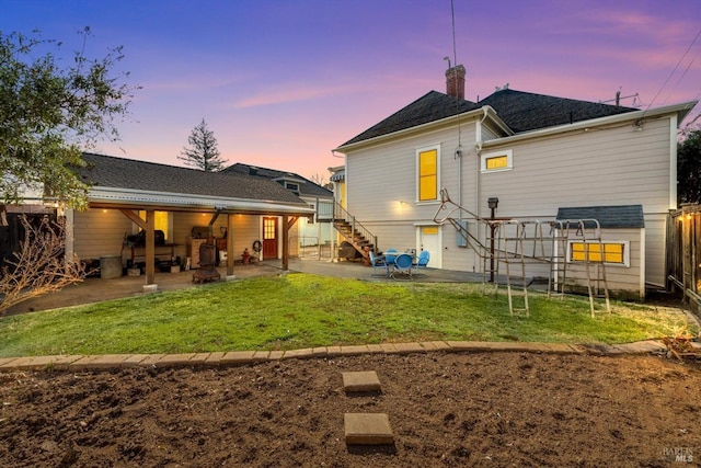 back of property at dusk with fence, stairs, a lawn, a chimney, and a patio area