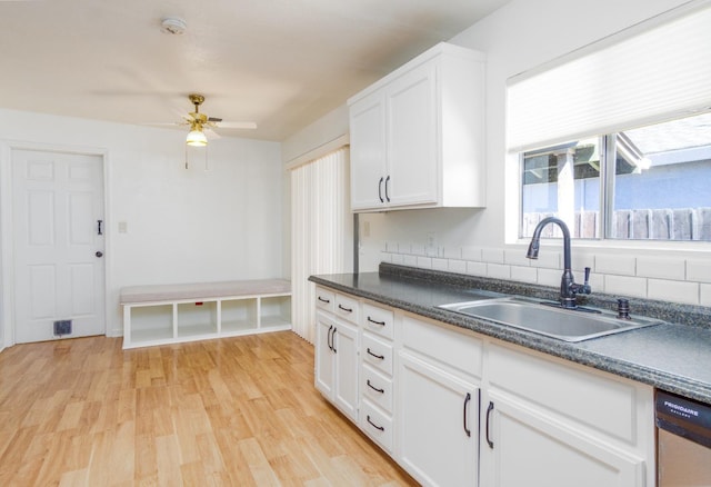 kitchen featuring white cabinetry, light wood-style flooring, a sink, dishwasher, and dark countertops