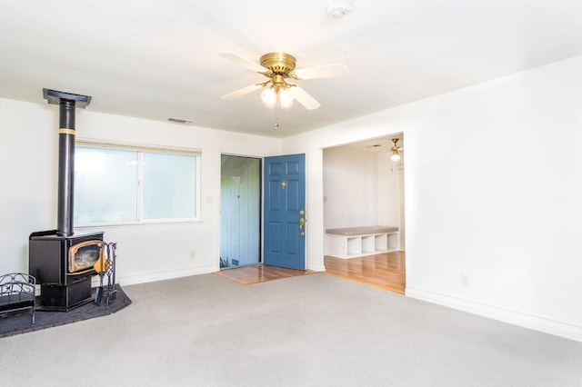 living area with a wood stove, carpet flooring, a ceiling fan, and visible vents