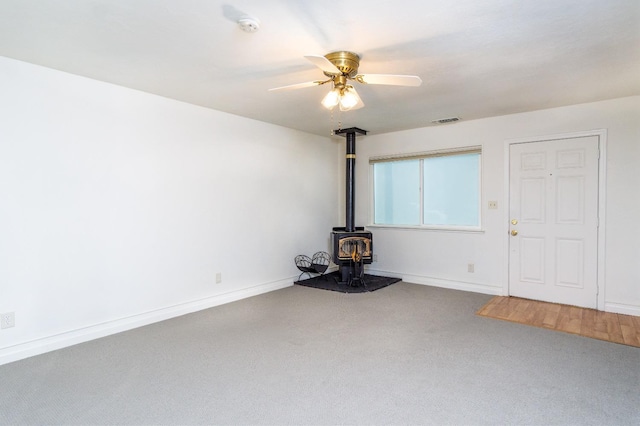 unfurnished living room with a ceiling fan, visible vents, baseboards, a wood stove, and carpet flooring