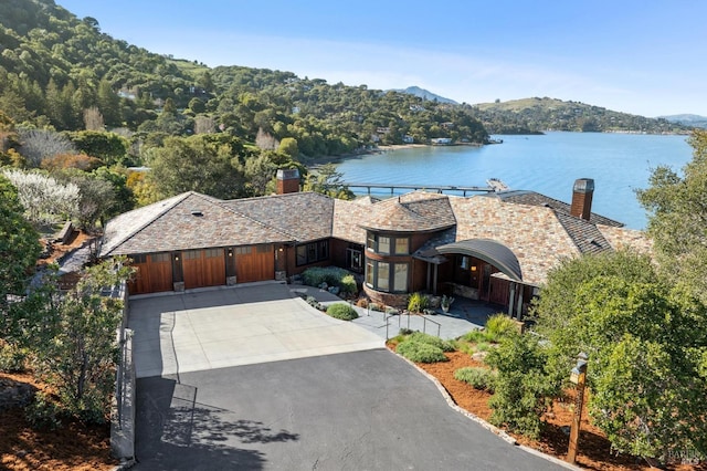 view of front of house featuring a garage, concrete driveway, a chimney, and a water and mountain view