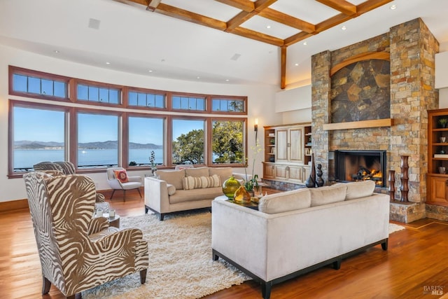 living room featuring beam ceiling, a high ceiling, a stone fireplace, wood finished floors, and baseboards