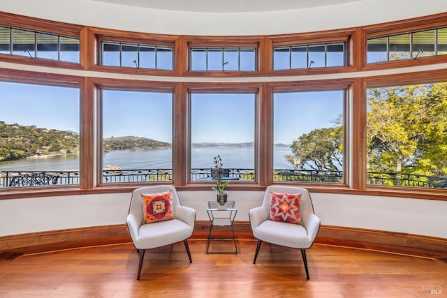 sitting room with a water view, visible vents, baseboards, and wood finished floors