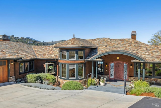 view of front of house with stone siding, a chimney, and a high end roof