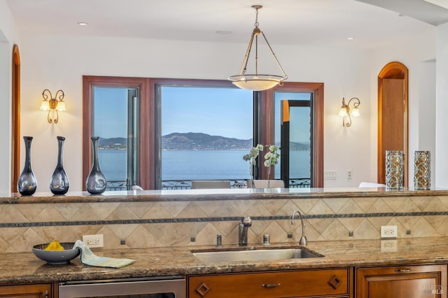 kitchen featuring stone countertops, arched walkways, brown cabinets, and a sink