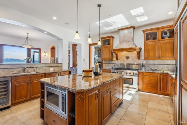 kitchen featuring arched walkways, wine cooler, a sink, appliances with stainless steel finishes, and custom range hood