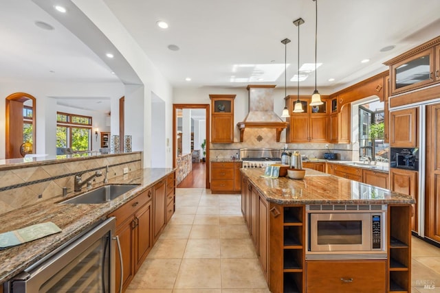 kitchen featuring brown cabinets, open shelves, a sink, built in appliances, and premium range hood