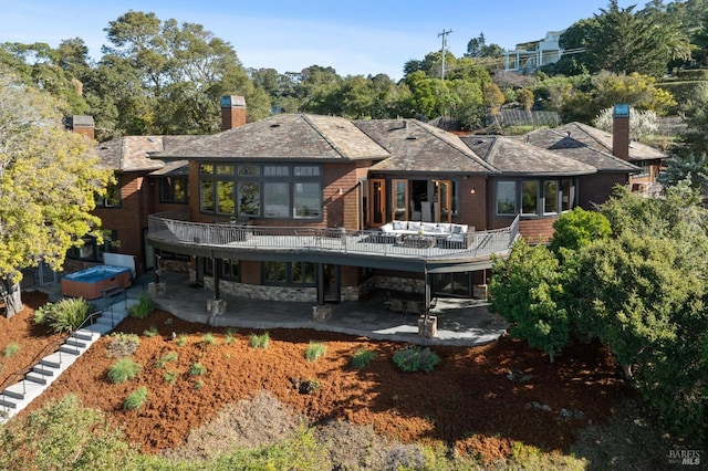 back of house featuring stone siding, a wooden deck, a chimney, and a patio