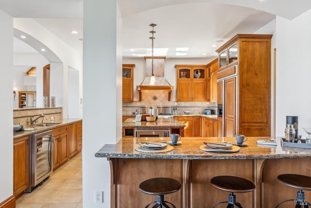 kitchen with dark stone countertops, beverage cooler, brown cabinetry, and custom exhaust hood