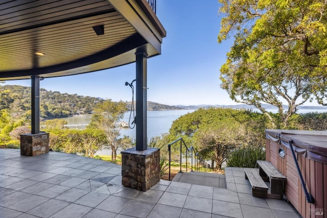 view of patio with a water view and a hot tub