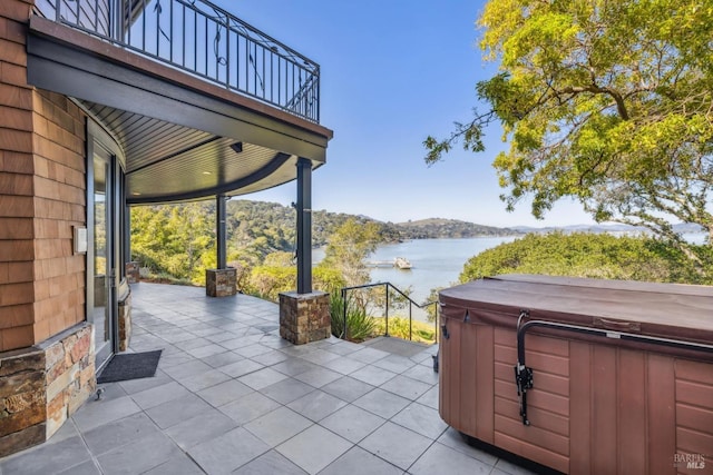 view of patio with a water view, a balcony, and a hot tub