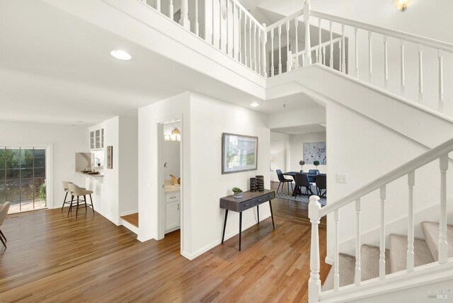 stairway featuring a high ceiling, recessed lighting, wood finished floors, and baseboards