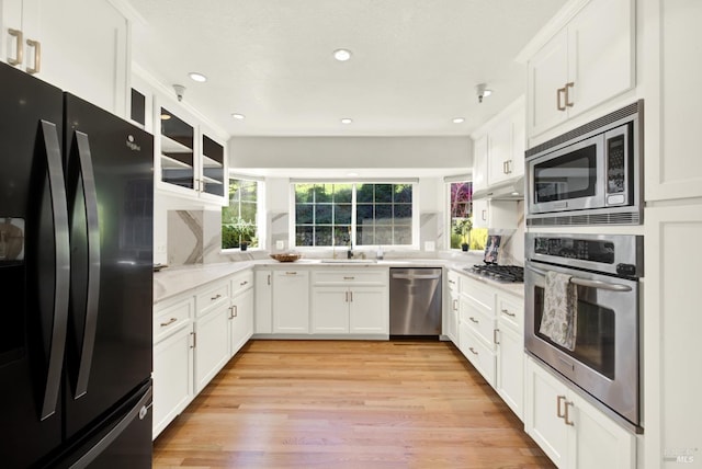 kitchen featuring glass insert cabinets, light wood finished floors, white cabinetry, and appliances with stainless steel finishes