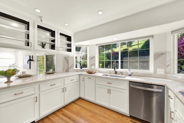 kitchen with a sink, light stone counters, white cabinets, and dishwasher