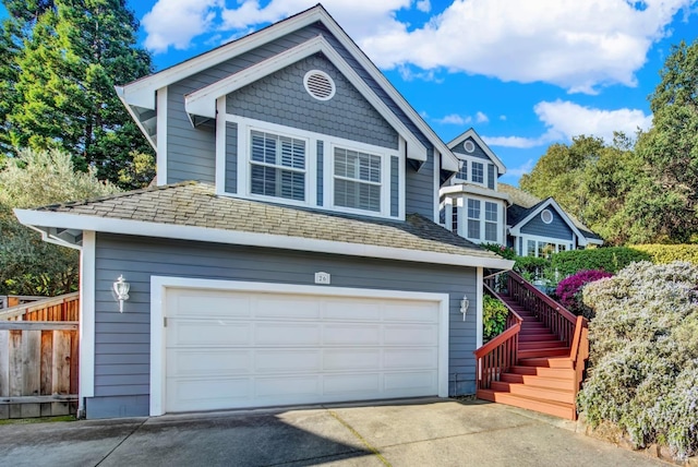 view of front of house featuring driveway, a shingled roof, stairs, and fence