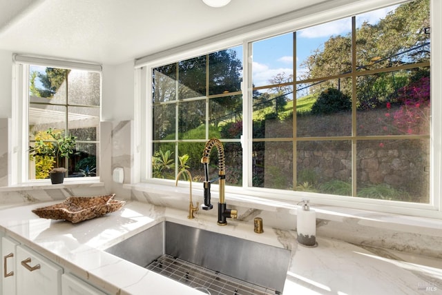 interior details with a sink, white cabinetry, and light stone countertops