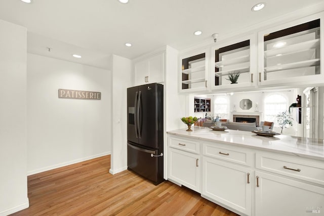 kitchen with white cabinets, light wood-style flooring, glass insert cabinets, black refrigerator with ice dispenser, and recessed lighting