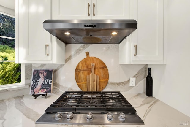 kitchen with ventilation hood, decorative backsplash, light stone countertops, and white cabinets