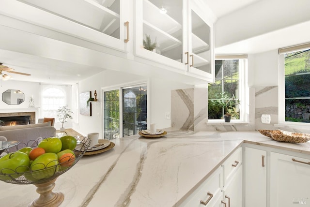 kitchen featuring a warm lit fireplace, glass insert cabinets, a wealth of natural light, and light stone countertops