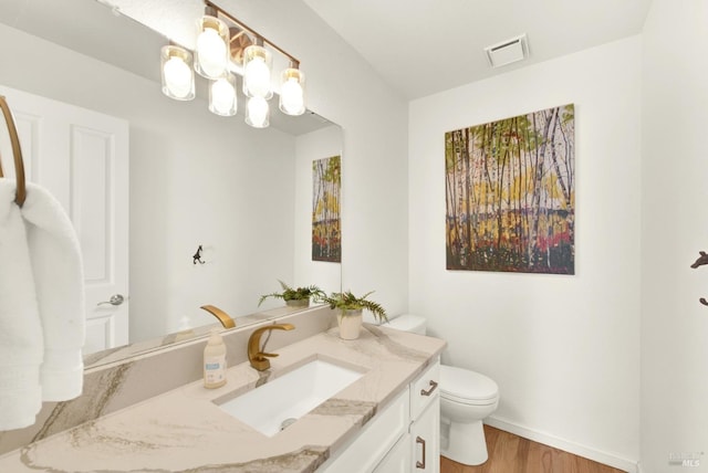 half bath with visible vents, toilet, vanity, wood finished floors, and baseboards