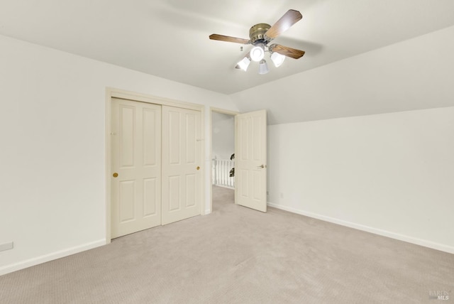 unfurnished bedroom featuring a closet, light colored carpet, vaulted ceiling, ceiling fan, and baseboards