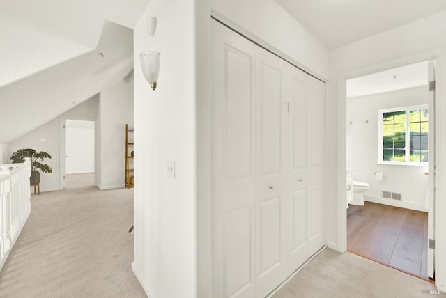 hall featuring light colored carpet, visible vents, light wood-style flooring, vaulted ceiling, and baseboards