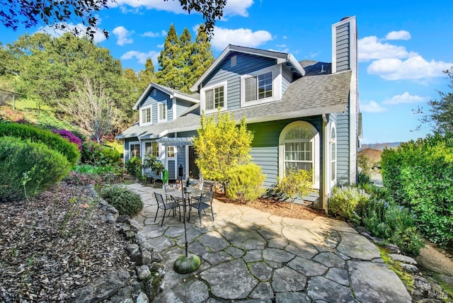 back of property with a shingled roof, a chimney, and a patio area