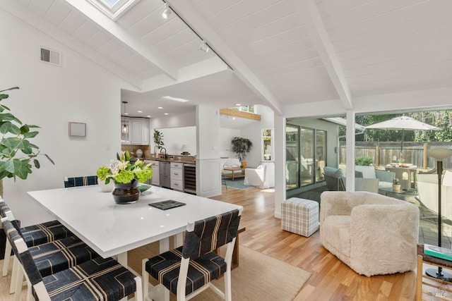 dining room with light wood finished floors, visible vents, wine cooler, vaulted ceiling with beams, and rail lighting