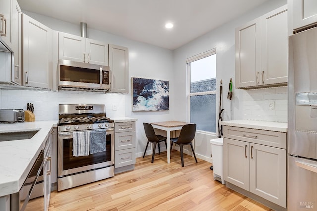 kitchen with gray cabinetry, baseboards, appliances with stainless steel finishes, light wood-type flooring, and backsplash