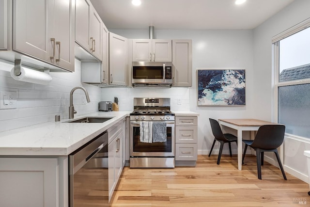 kitchen with stainless steel appliances, light wood-type flooring, a sink, and gray cabinetry