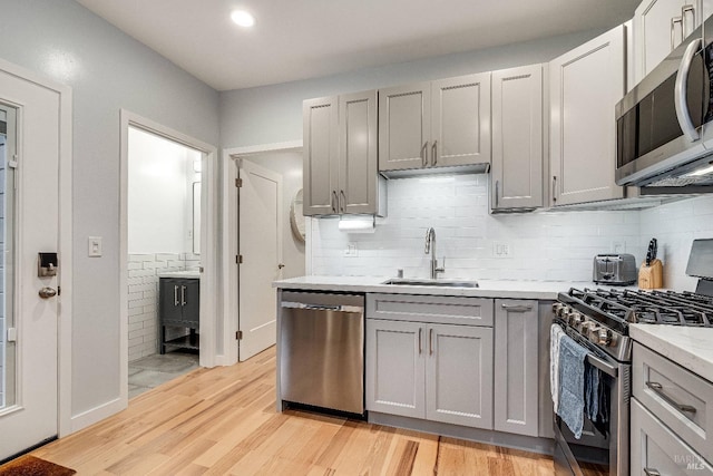 kitchen with light countertops, appliances with stainless steel finishes, a sink, and gray cabinetry