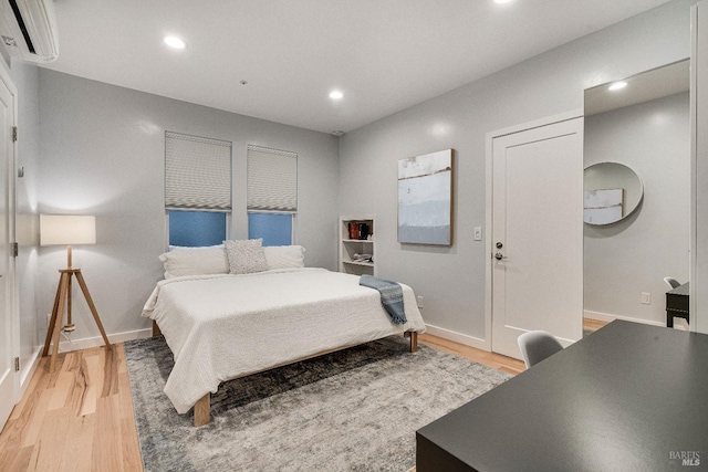 bedroom featuring recessed lighting, baseboards, a wall mounted air conditioner, and light wood finished floors