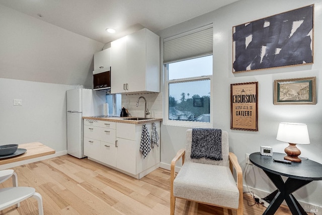 kitchen with light wood-style flooring, a sink, baseboards, white cabinets, and tasteful backsplash