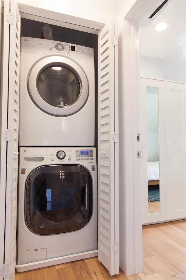 clothes washing area featuring light wood-type flooring, stacked washer and dryer, visible vents, and laundry area