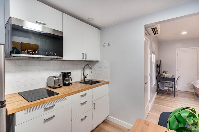 kitchen with black electric cooktop, wood counters, a sink, backsplash, and stainless steel microwave