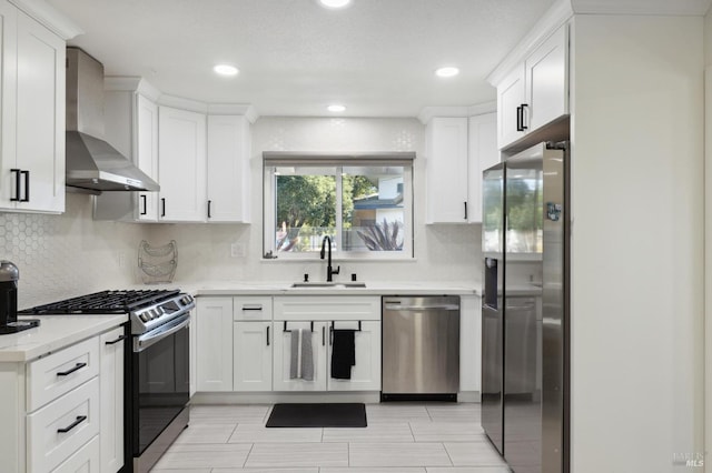 kitchen featuring wall chimney exhaust hood, appliances with stainless steel finishes, a sink, and white cabinetry