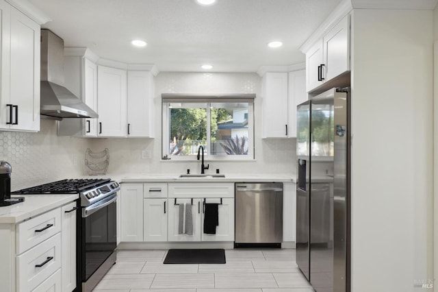 kitchen with tasteful backsplash, wall chimney range hood, white cabinets, appliances with stainless steel finishes, and a sink