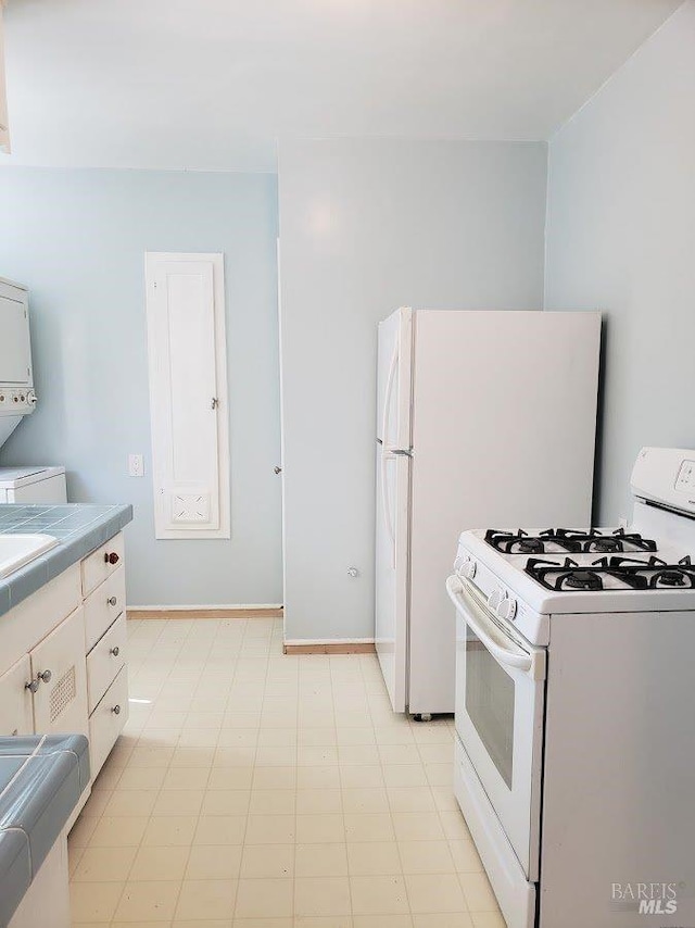 kitchen with stacked washer and dryer, white appliances, light floors, and a sink