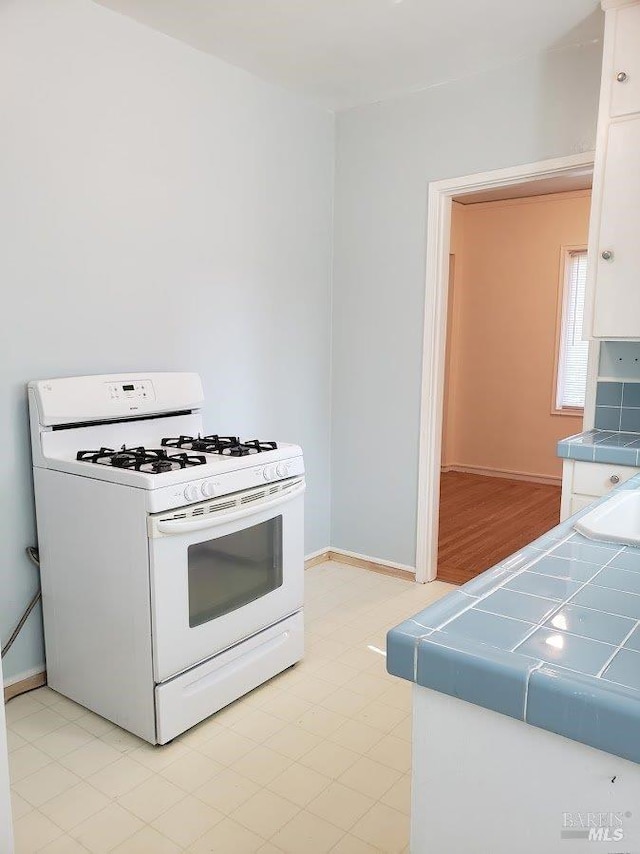 kitchen with white cabinetry, white gas range, tile counters, and baseboards