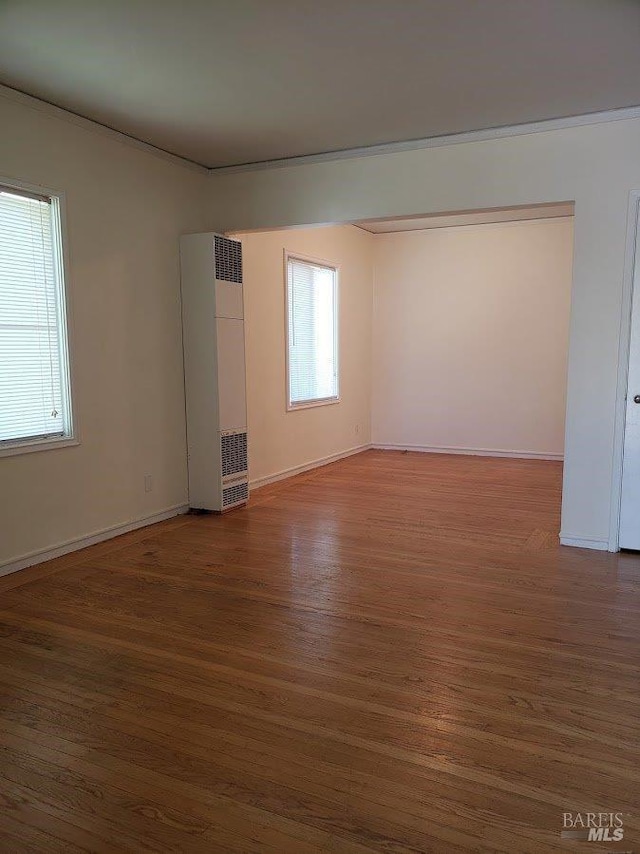 empty room with baseboards, wood finished floors, and a healthy amount of sunlight