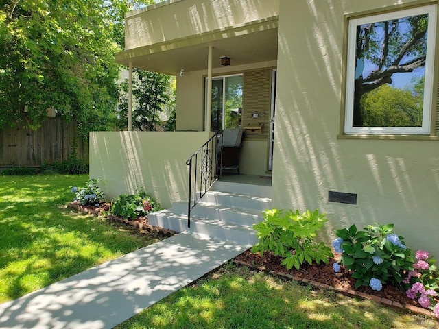 entrance to property with fence, a lawn, and stucco siding