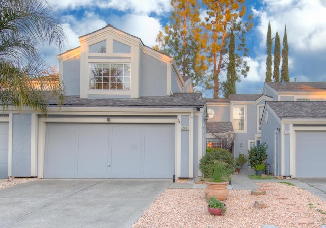 view of front of property featuring concrete driveway, roof with shingles, an attached garage, and stucco siding