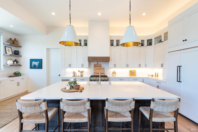 kitchen featuring custom range hood, a center island with sink, light countertops, and light wood-style flooring