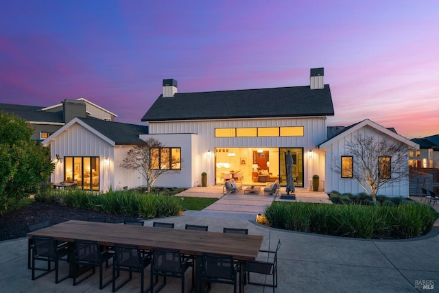 back of property at dusk with a patio, outdoor dining space, board and batten siding, and a chimney