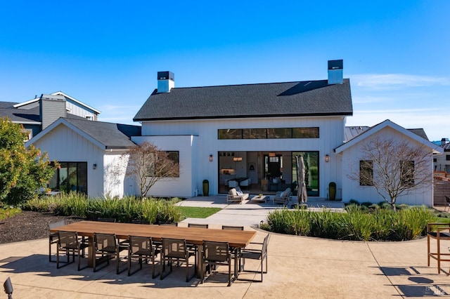 back of house with a patio, a shingled roof, and a chimney