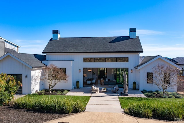 rear view of house with a patio area, a chimney, and roof with shingles