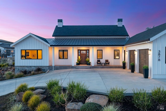 back of property at dusk featuring a standing seam roof, a chimney, metal roof, and board and batten siding