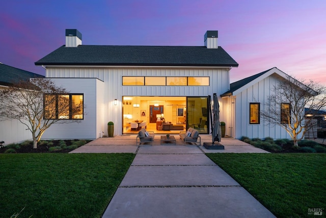 back of property with a patio, board and batten siding, a chimney, and a lawn