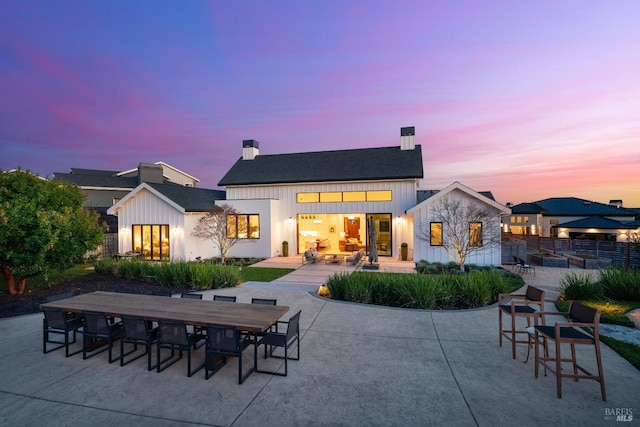 back of property at dusk with board and batten siding, outdoor dining area, and a patio